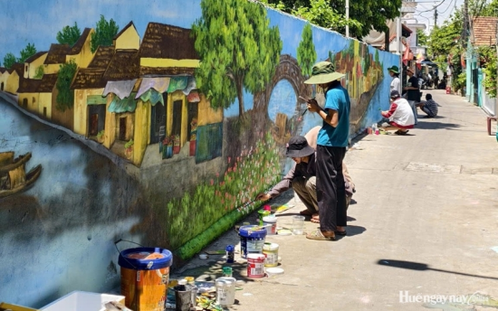 The Cau Hamlet mural, showing a bridge, a riverside landing stage, and houses along the river, was gradually taking shape